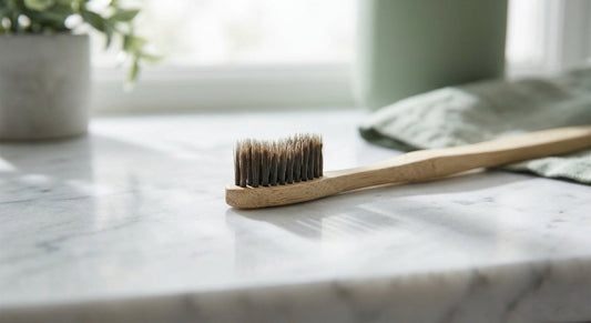 A single bamboo toothbrush photographed in close detail on a white marble surface under soft natural light, highlighting its bristles.
