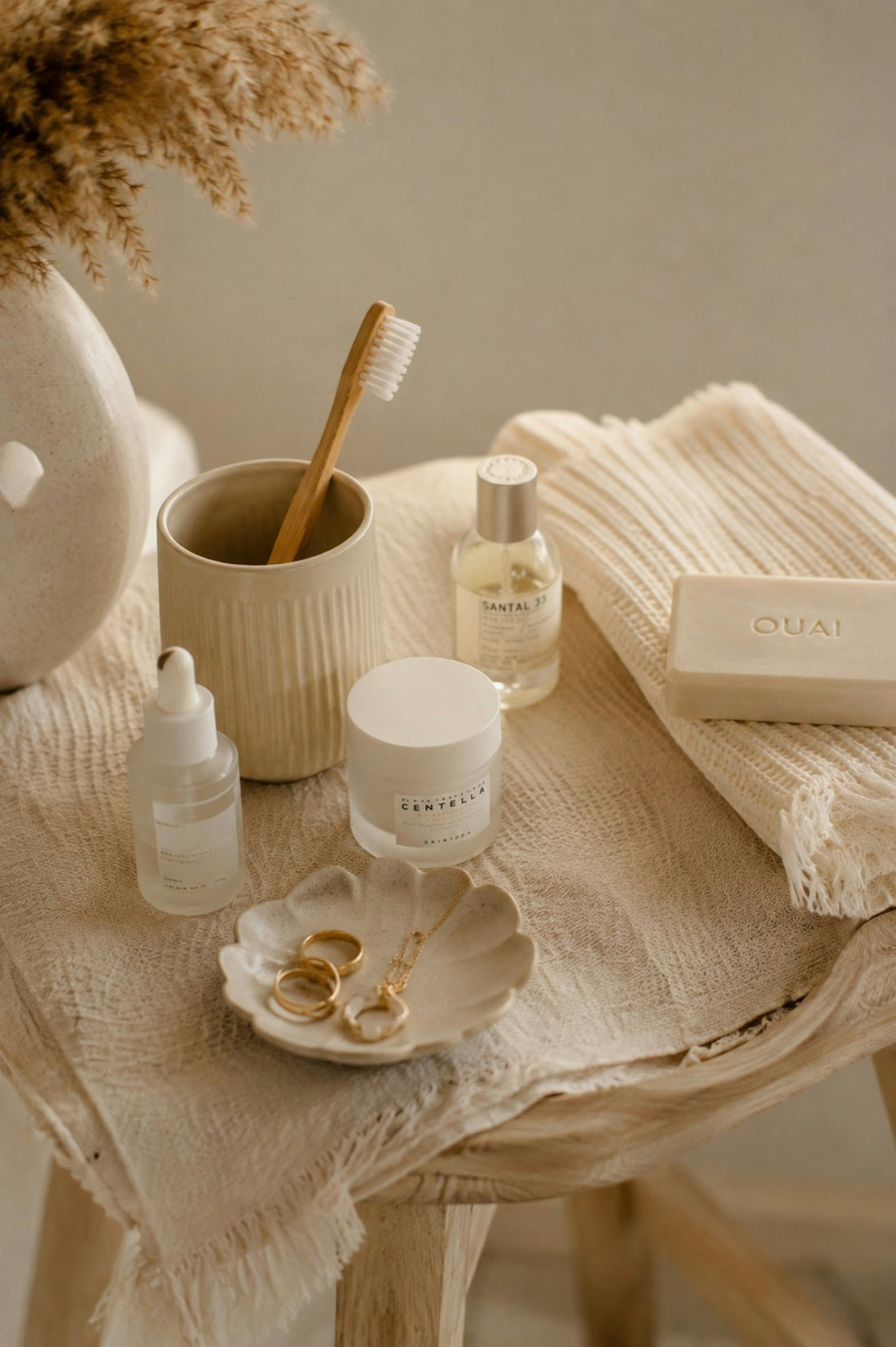 Skincare products, a bamboo toothbrush, and jewelry on a textured cloth surface