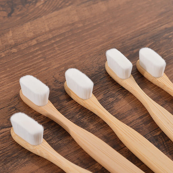 Set of five eco-friendly bamboo toothbrushes with soft, white bristles on a wooden surface.